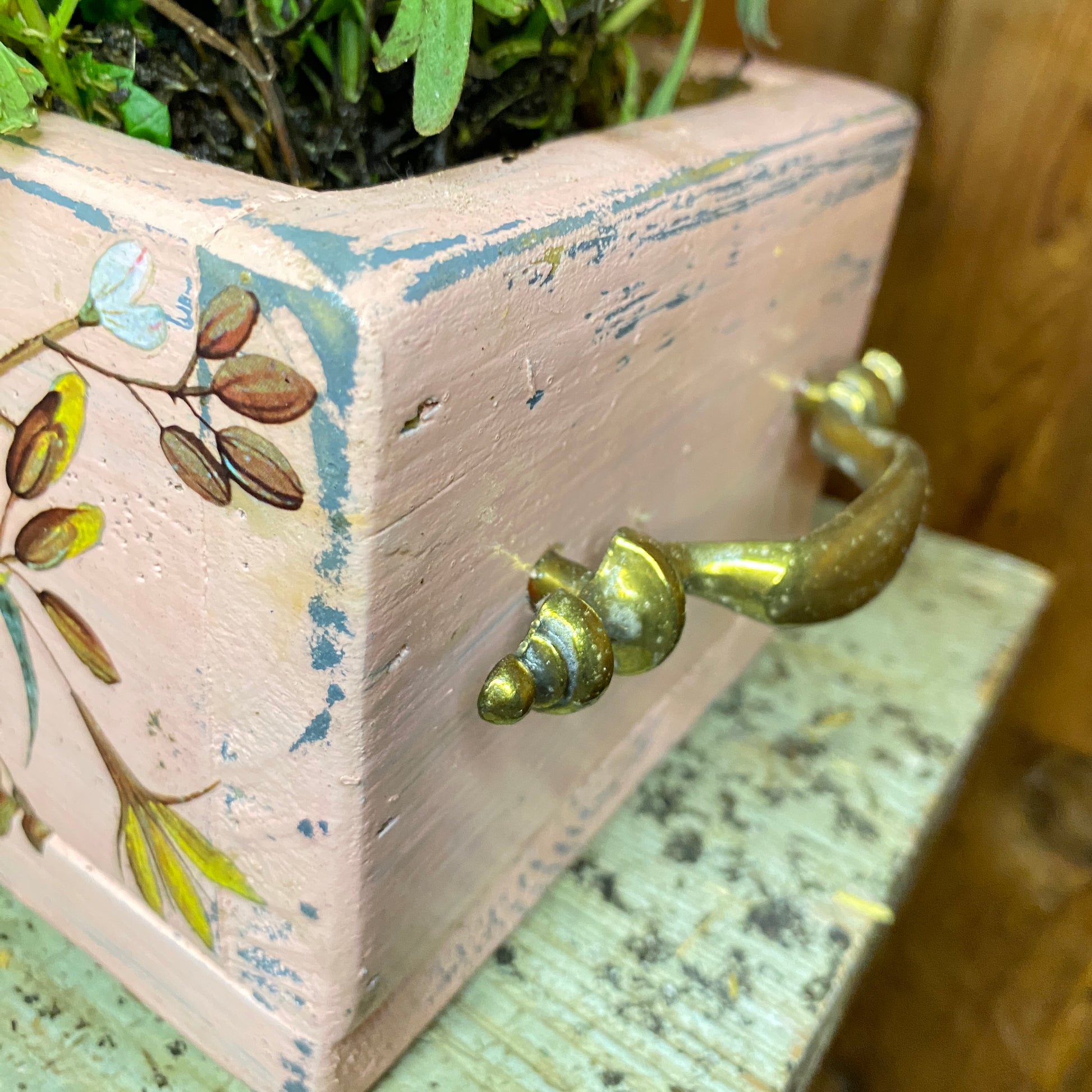 Wooden box with floral design and brass handle on a textured surface