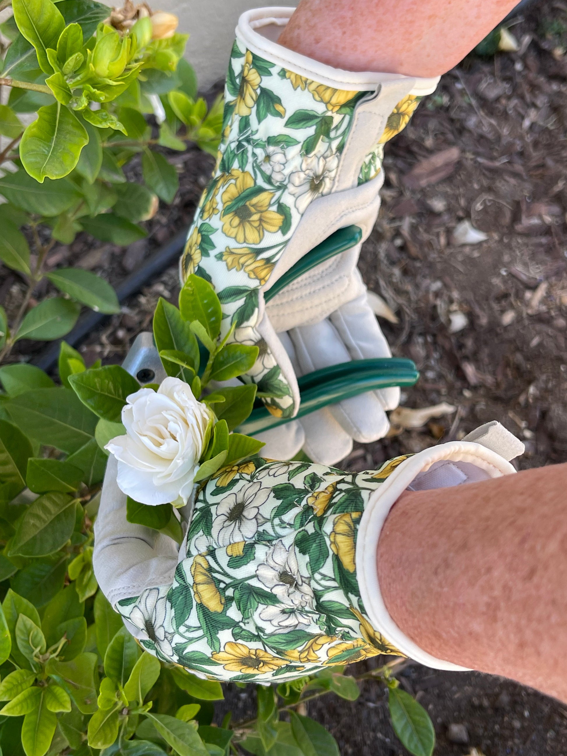 Gardening gloves with floral pattern holding a white flower in a garden setting
