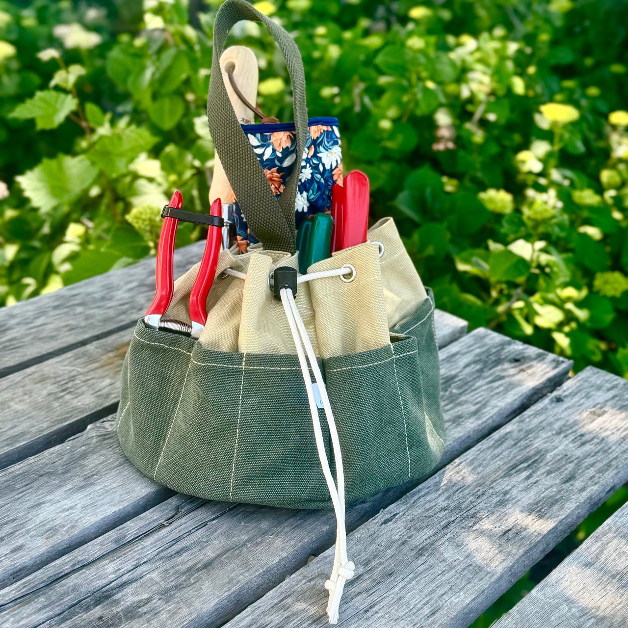 Green tool belt with tools on a wooden surface with a green leafy background
