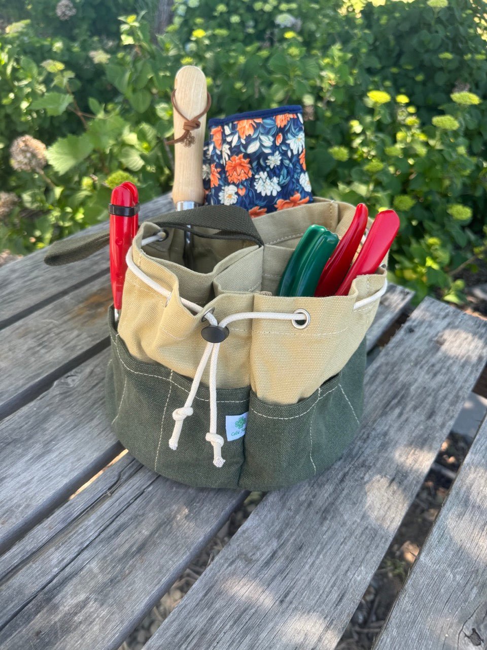 Green tool roll with gardening tools on a wooden surface with greenery in the background