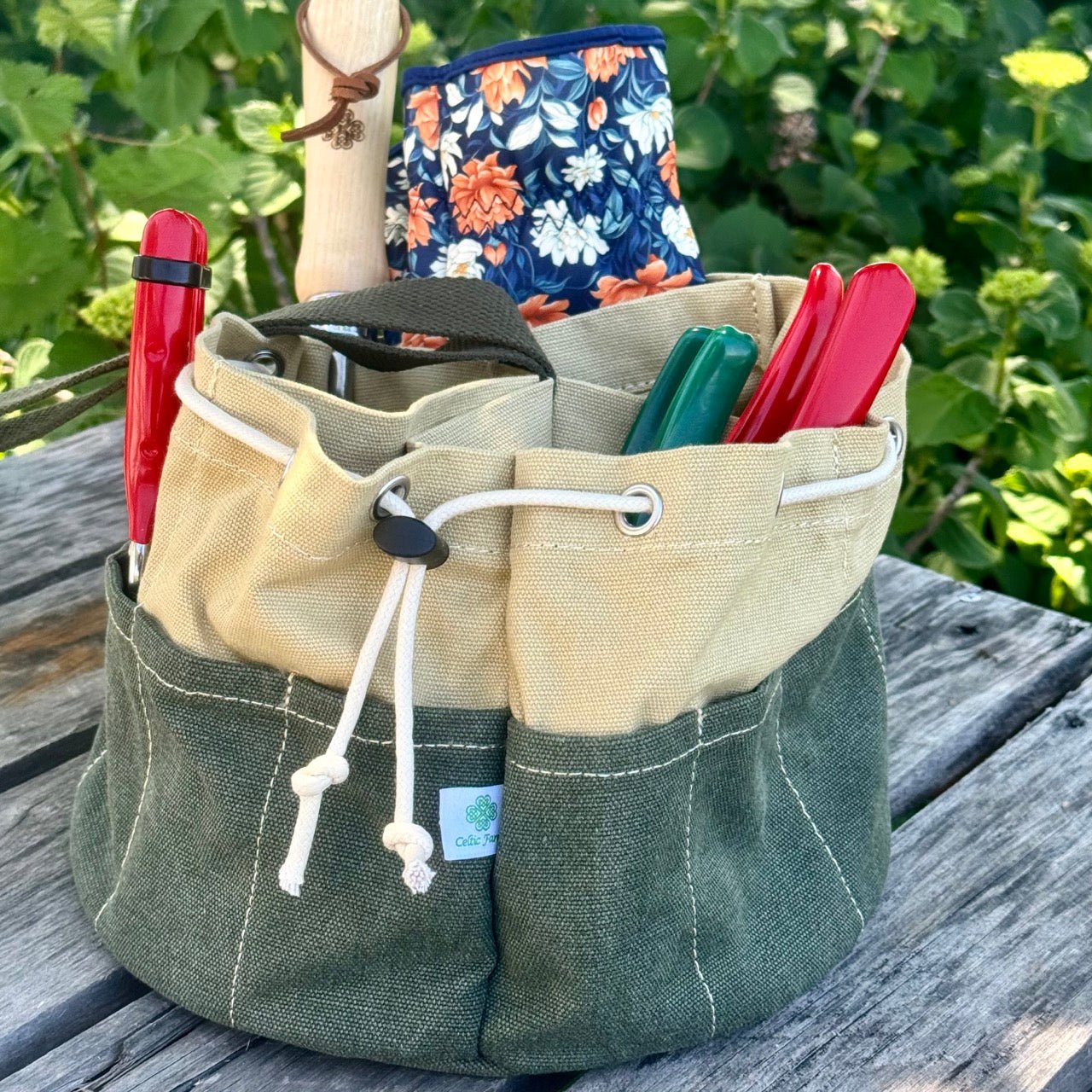 Green and beige multi-tool pouch with tools on a wooden surface with greenery in the background