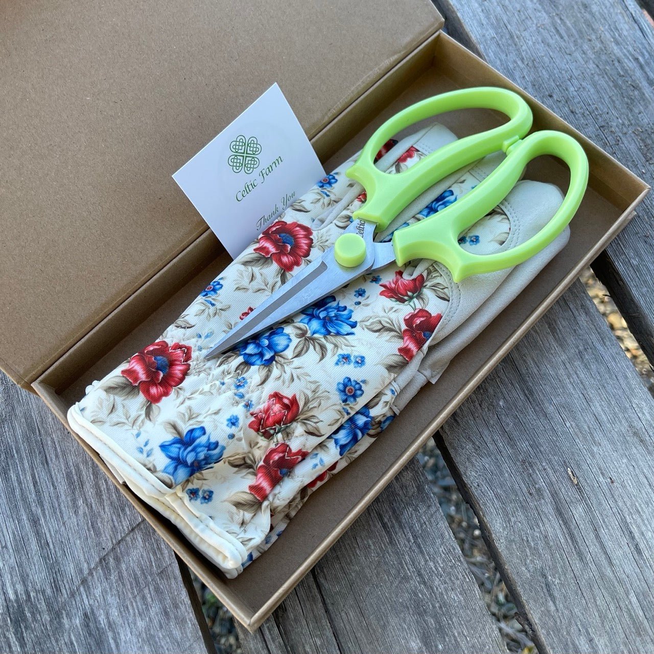 Floral-patterned shears in a box with a visible brand label on a wooden surface