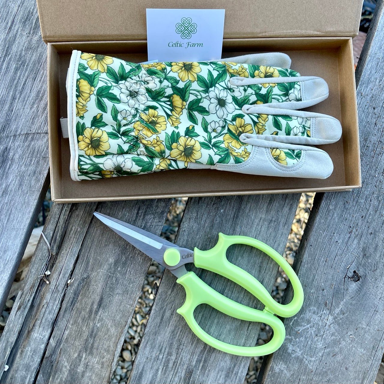 Floral gardening gloves and green-handled scissors in a box on a wooden surface