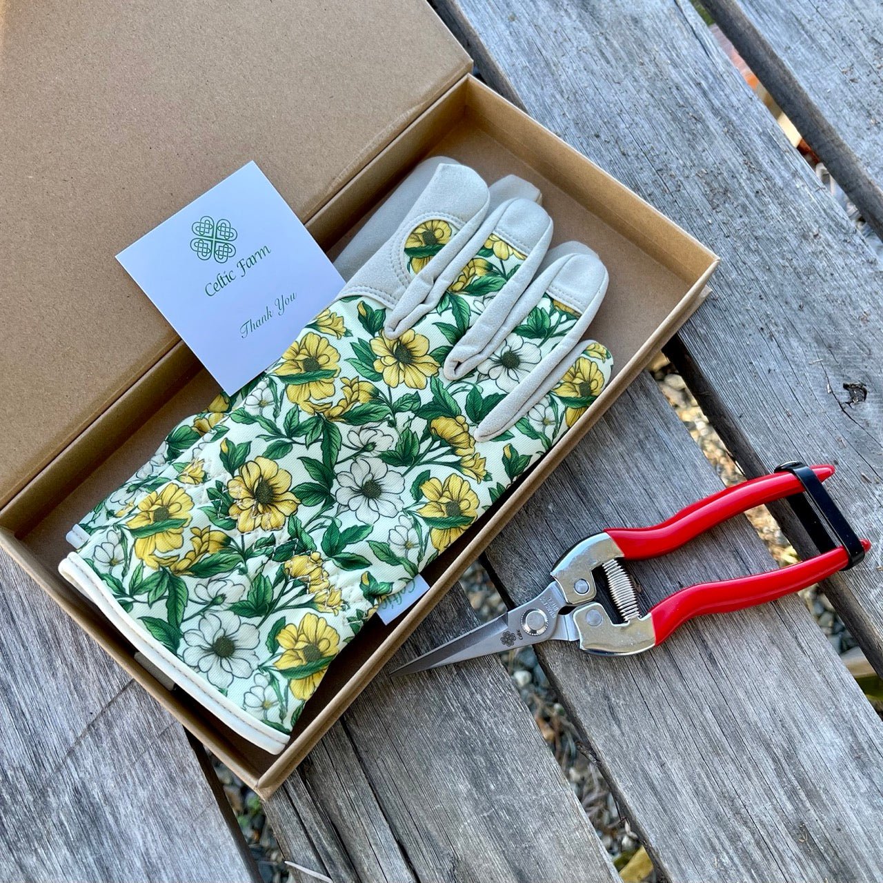 Floral gardening gloves in a box with a pair of pruners on a wooden surface