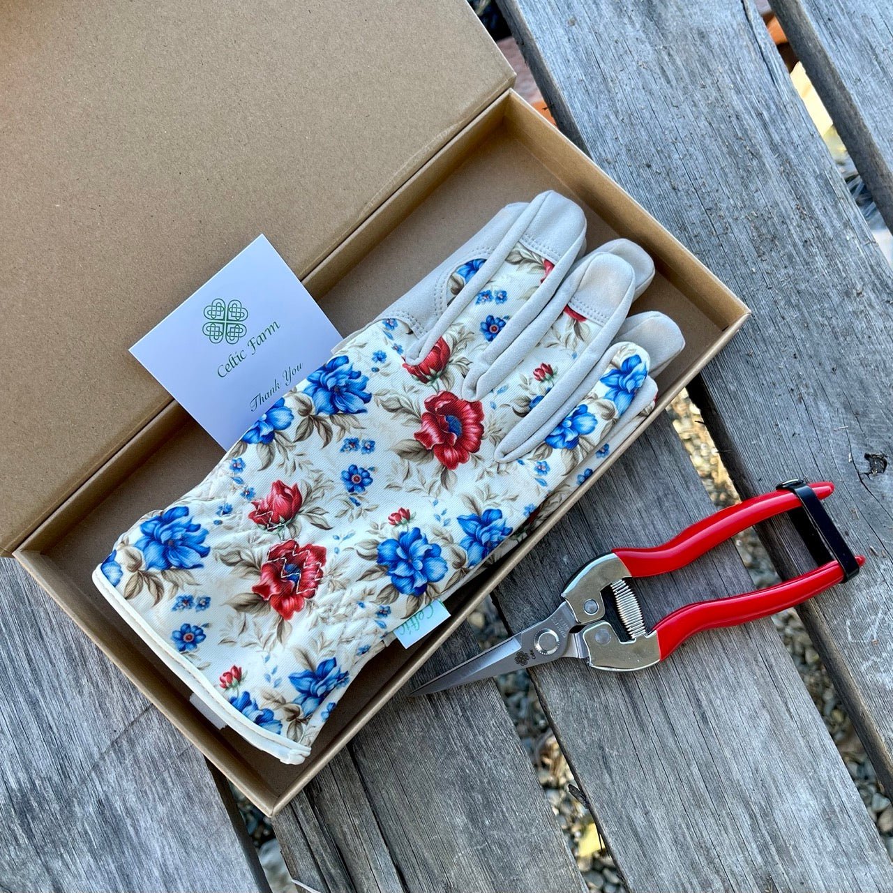 Floral-patterned gardening gloves in a box with a pair of scissors on a wooden surface.