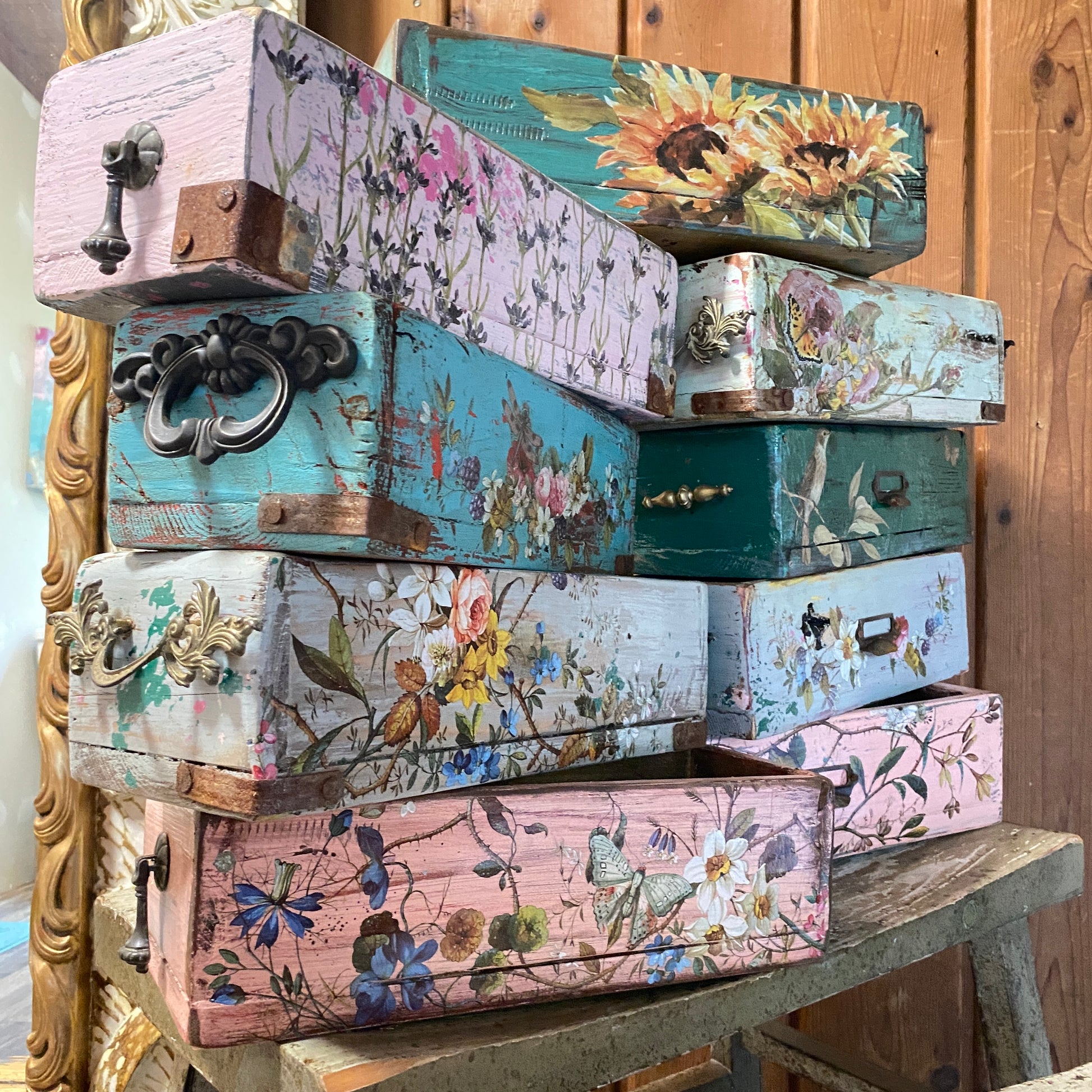 Stack of decorative wooden boxes with floral patterns on a wooden surface.